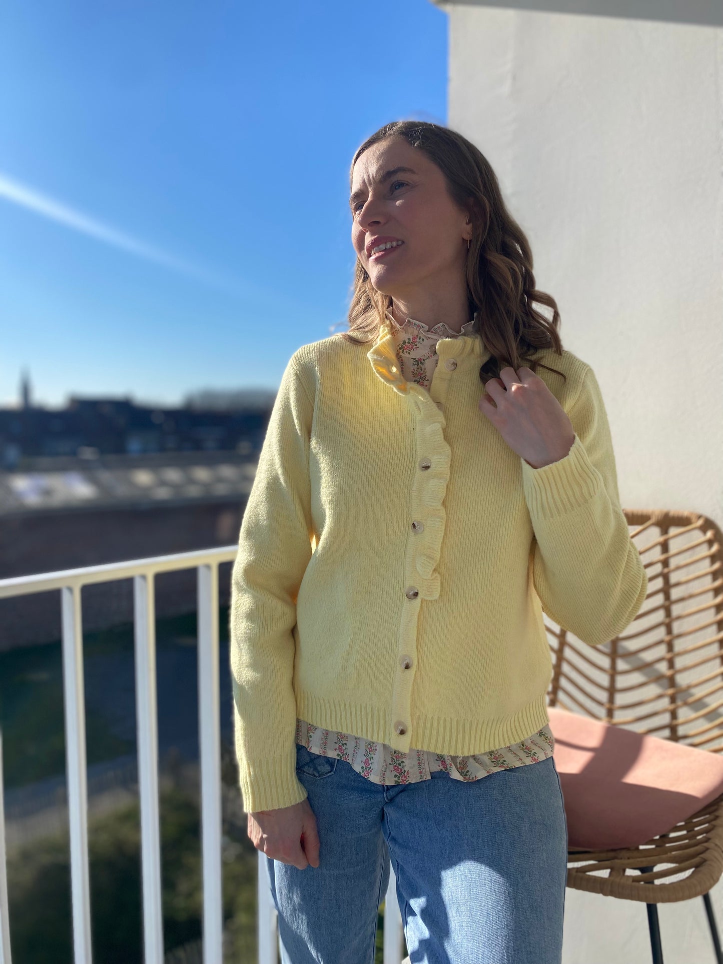 Femme portant le gilet Freda jaune pastel à volants sur une blouse fleurie, style printanier.