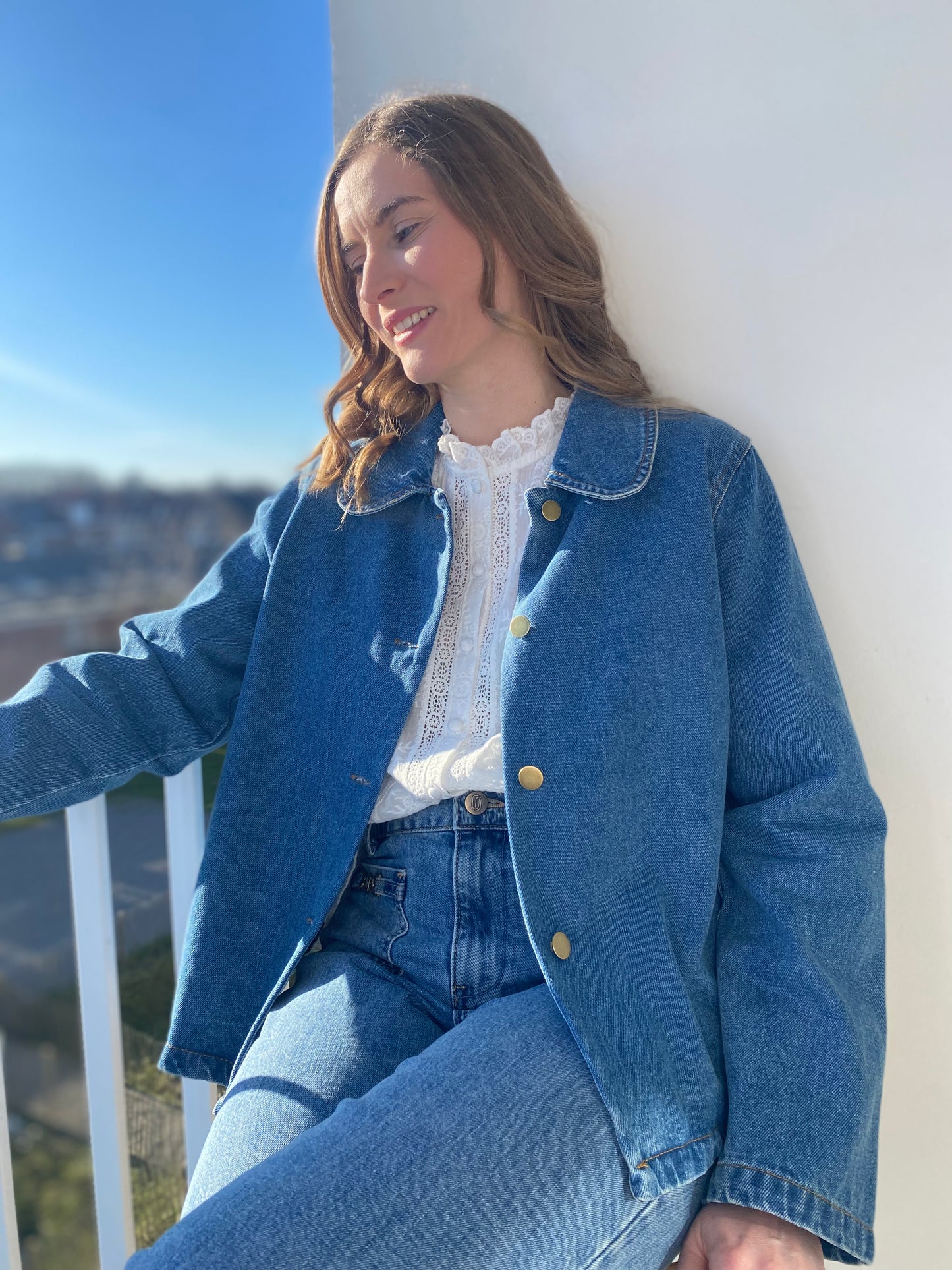 Femme portant la veste en jean Rosalie bleue avec boutons dorés sur une blouse blanche.