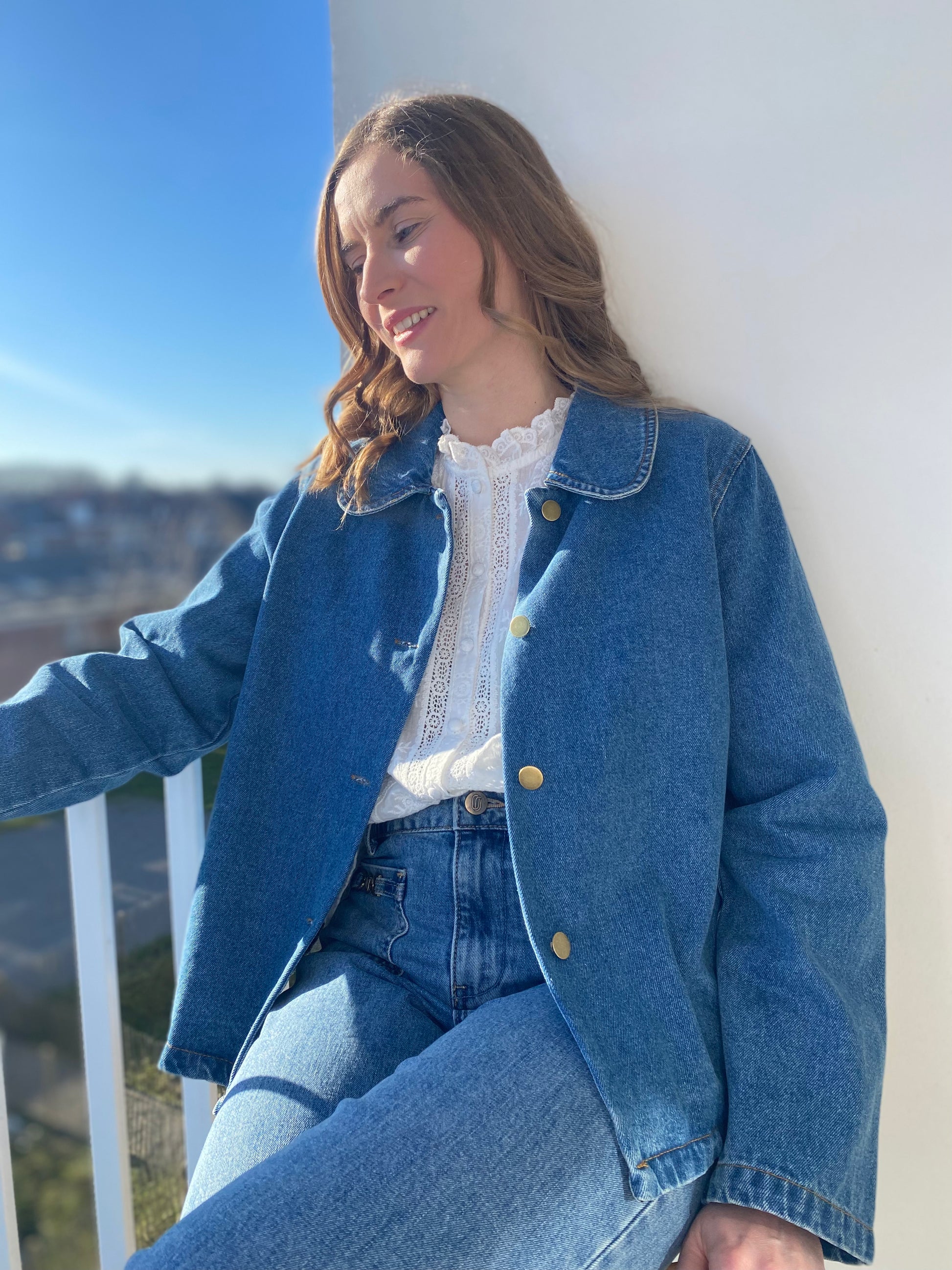 Femme portant la veste en jean Rosalie bleue avec boutons dorés sur une blouse blanche.