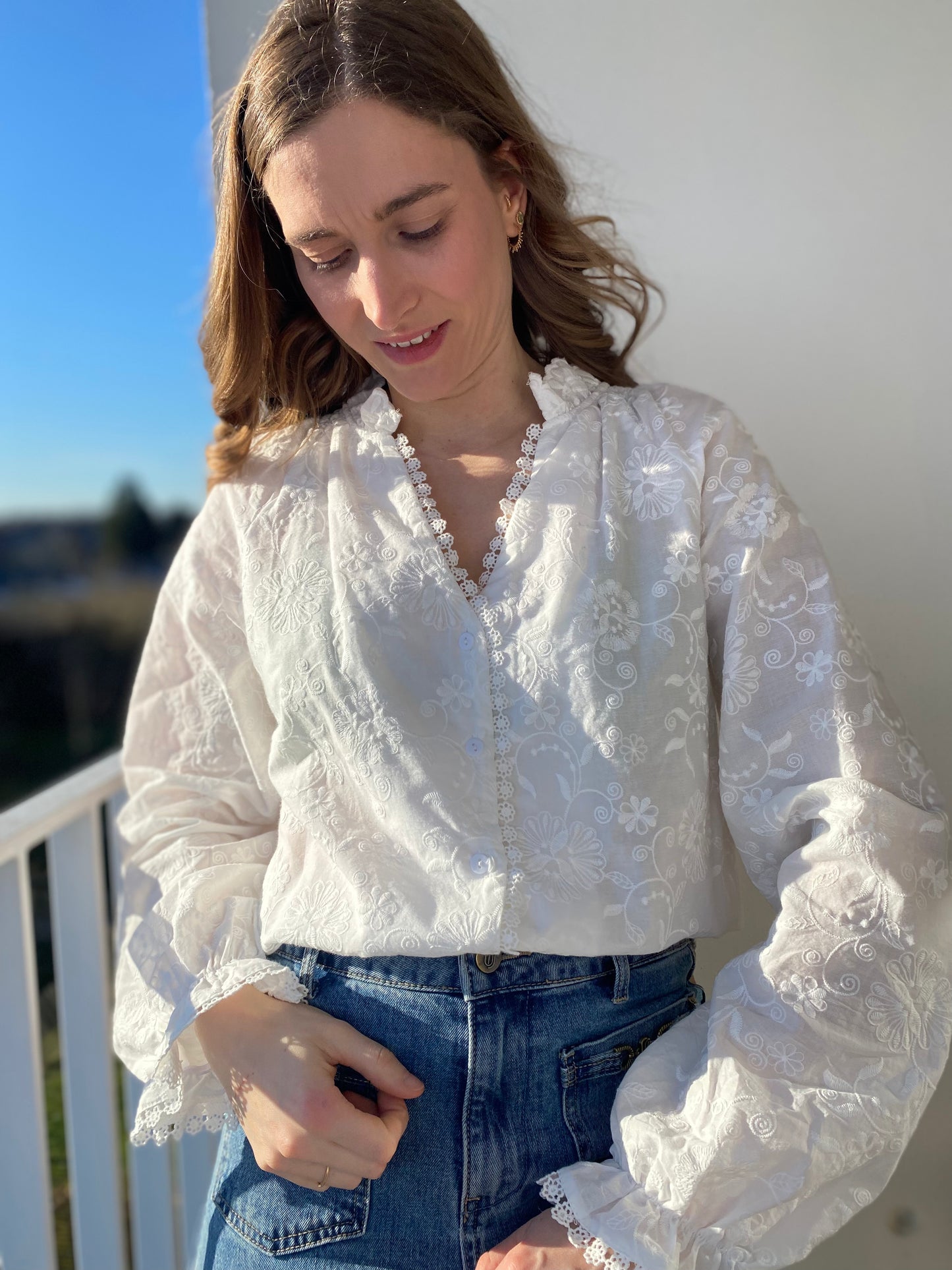 Femme portant une blouse blanche brodée transparente avec col en V dentelé et manches à volants sur un jean.