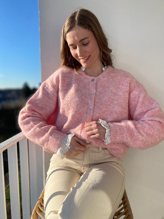 Femme portant le gilet Lala rose chiné sur une blouse blanche en dentelle, look doux de printemps.