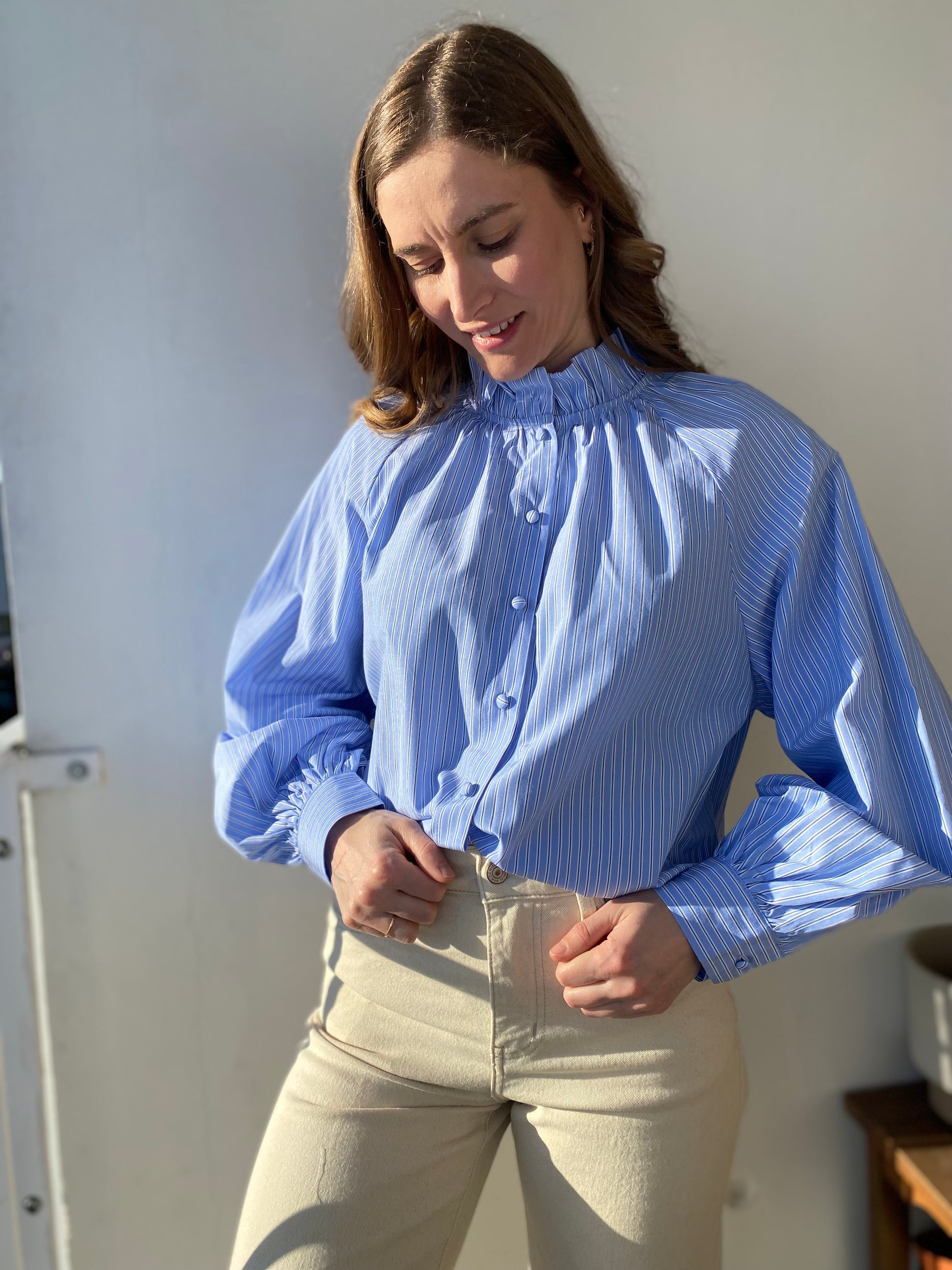 Femme portant la chemise Annie bleue à rayures blanches avec col froncé et manches bouffantes.